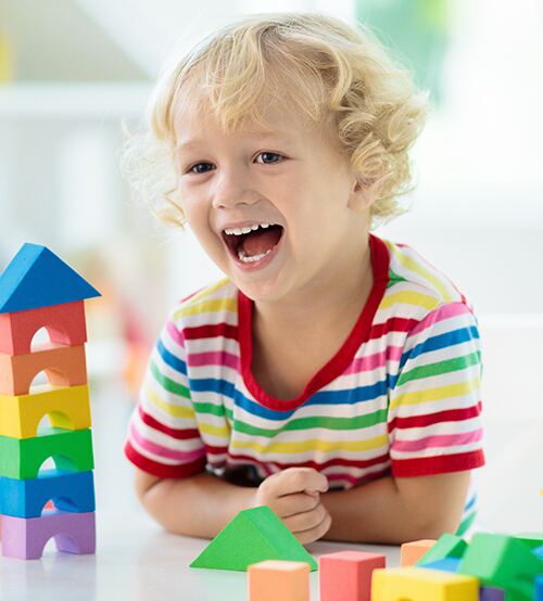 Cheerful laughing child building colorful blocks indoors with hands on a playful tabletop