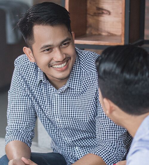 Smiling man in blue checkered shirt conversing with another man indoors