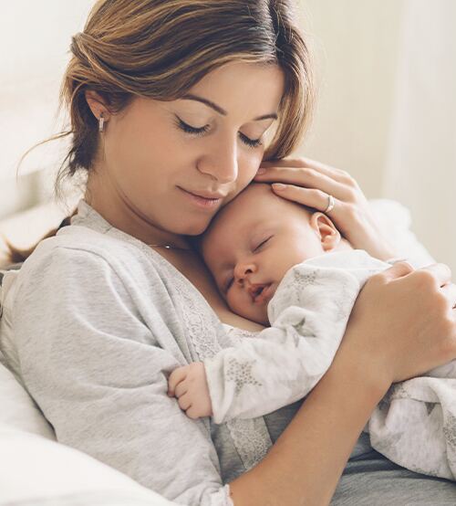 Tender mother cradles newborn baby in soft morning light, peaceful bonding and love.