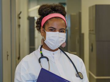 Masked nurse with stethoscope in clinic hallway, centered and professional healthcare worker
