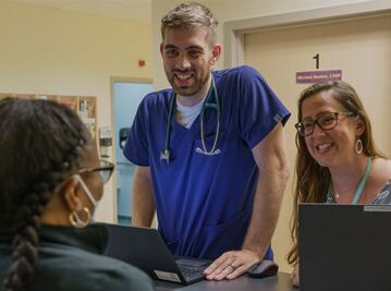 Doctor in blue scrubs consults with smiling nurse and patient in clinic room 1
