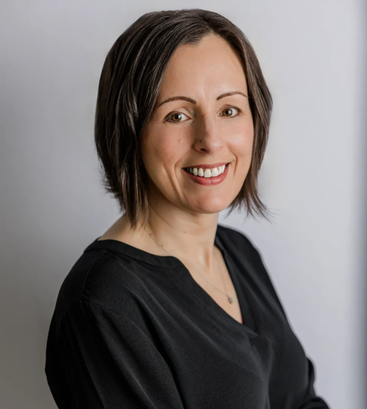Warm smiling woman headshot in black studio top against light neutral background