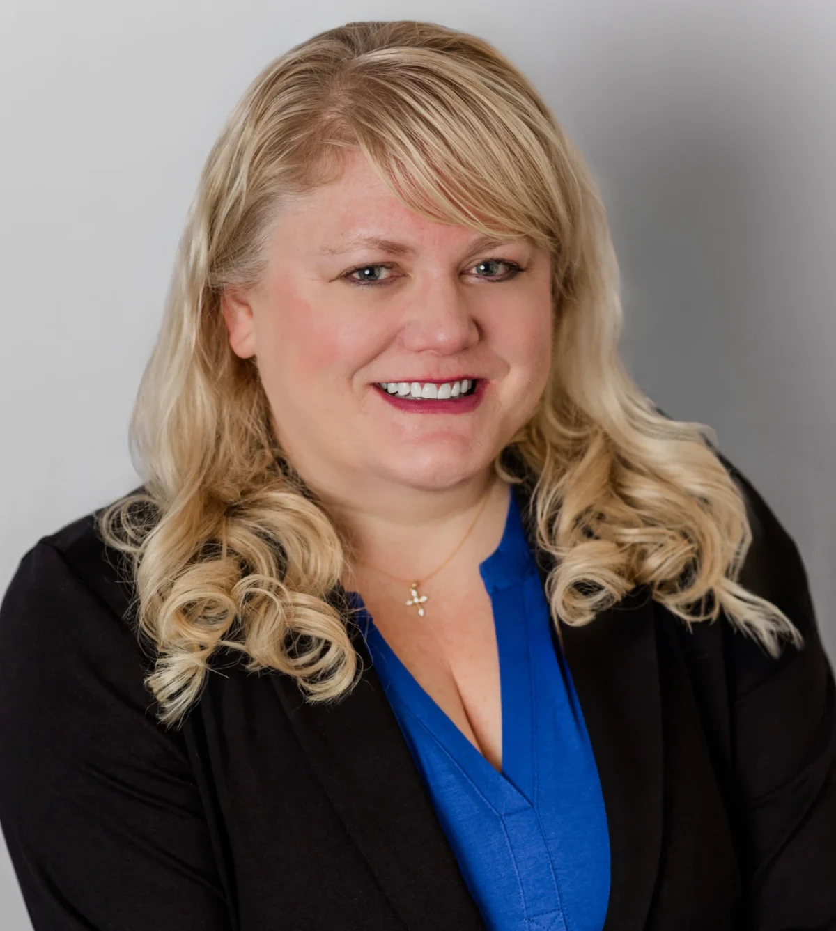 Smiling blonde professional headshot in royal blue blouse and dark blazer