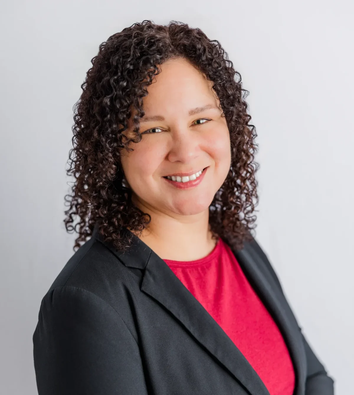 Curly-haired woman smiling in dark blazer and bright pink top professional headshot