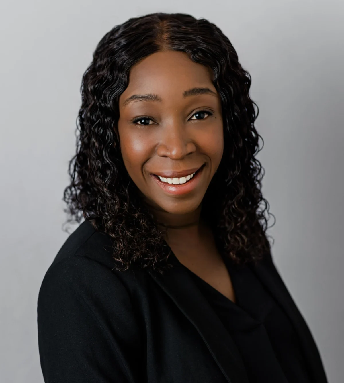 Warm smiling professional woman with voluminous curly hair in a black blazer headshot