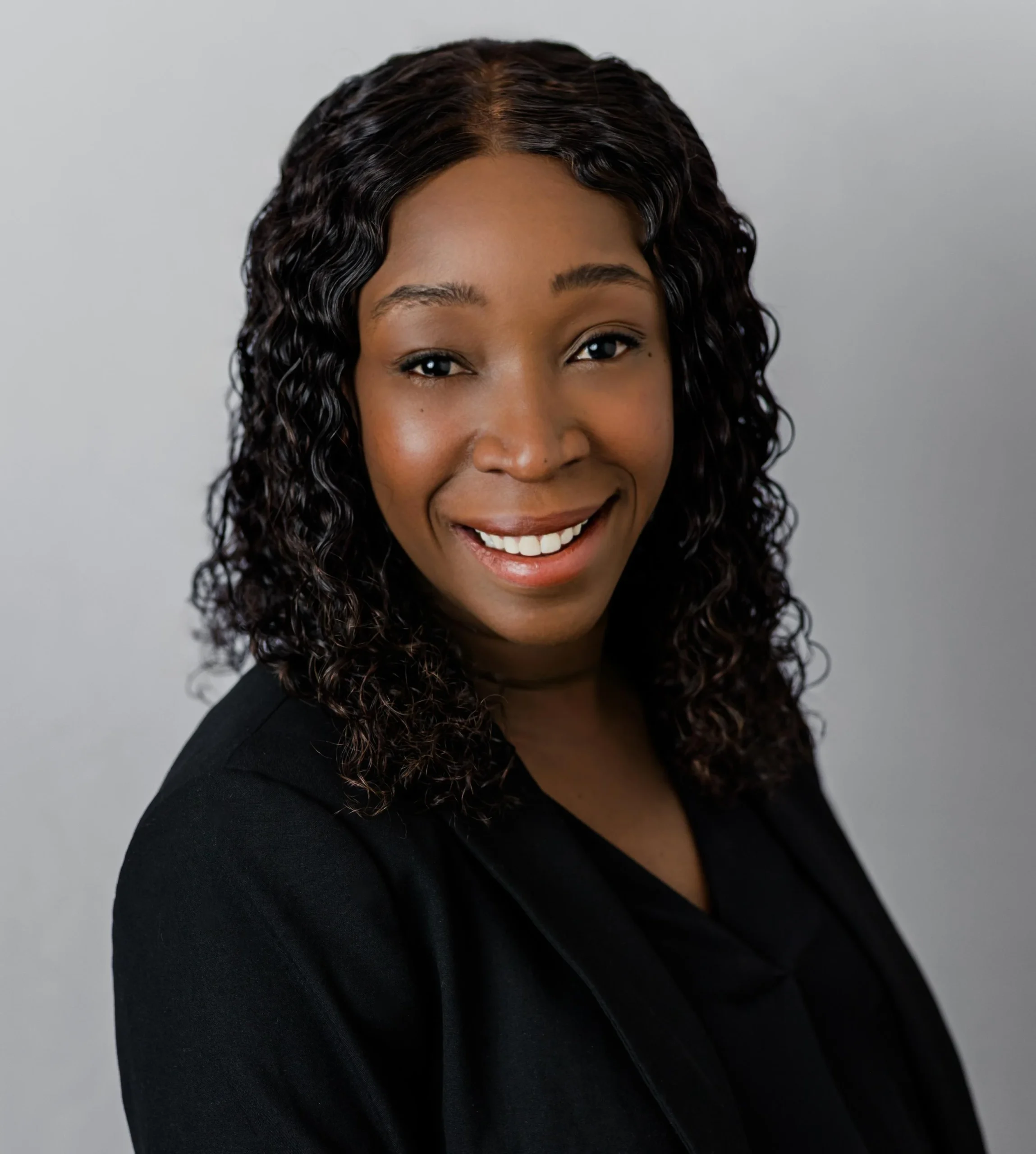 Warm smiling professional woman with voluminous curly hair in a black blazer headshot